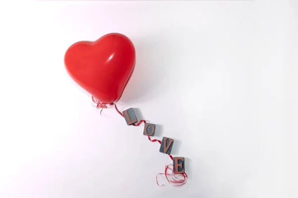 A red heart shaped balloon and red string with letters for the word love on a white background