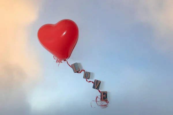 A red heart shaped balloon and red string with letters for the word love on a light blue background
