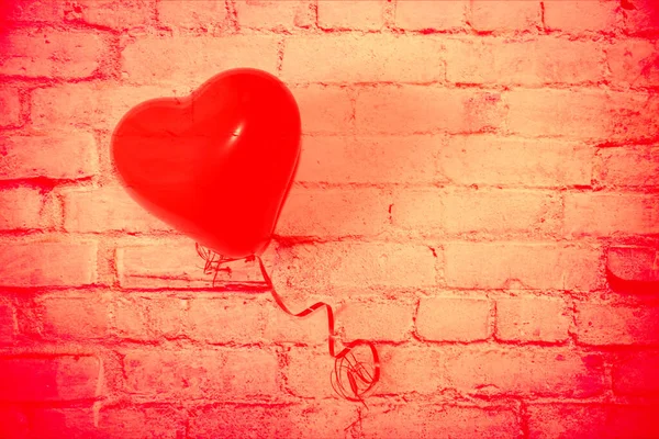 A red heart shaped balloon with red string, with a stone wall in red tone