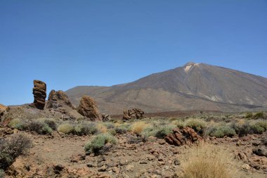 İspanya 'nın Tenerife Kanarya Adası' ndaki Teide Ulusal Parkı 'nda volkanik kayadan oluşan tuhaf şekilli Roque Cinchado kayası. Teide Dağı ve mavi gökyüzü manzaralı.