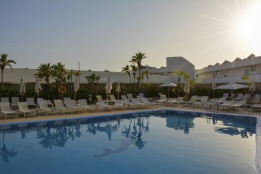 Akşam ışığında güneşli bir otelin havuzu ve palmiye ağaçları.