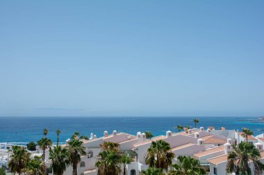 İspanya 'nın Costa Adeje kentindeki Tenerife Kanarya Adası' nda deniz kenarındaki bungalovlar ve palmiye ağaçları. La Gomera adası ufukta neredeyse hiç görünmüyor.