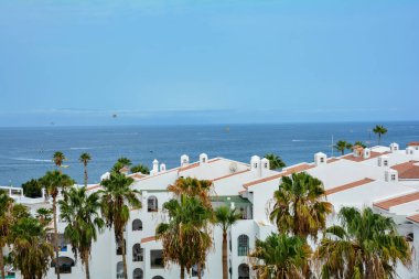 İspanya 'nın Costa Adeje kentindeki Tenerife Kanarya Adası' nda deniz kenarındaki bungalovlar ve palmiye ağaçları. La Gomera adası ufukta neredeyse hiç görünmüyor.