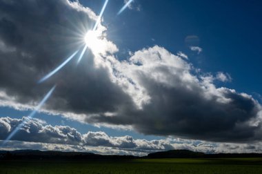 Kara bulutlar güneş ve yeşil manzarayla bir araya geliyor.