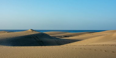 İspanya 'daki Gran Canaria' daki Maspaloma 'nın kumullarında. Mavi gökyüzü ile deniz manzarası. Dev kum tepeleri küçük bir çöle benzer ve doğa koruma alanıdır..