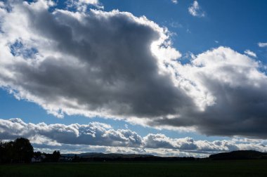 Mavi gökyüzü ve yeşil manzarayla kara bulutlar toplanıyor.