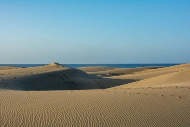 İspanya 'daki Gran Canaria' daki Maspaloma 'nın kumullarında. Mavi gökyüzü ile deniz manzarası. Dev kum tepeleri küçük bir çöle benzer ve doğa koruma alanıdır..