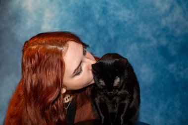 Mavi arka planı olan siyah kedisi olan bir kız.