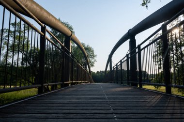 Metal ve tahta yaya köprüsünün yeşil doğadaki güneş ışığıyla görüntüsü