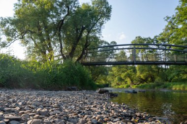 Nehir kıyısındaki çakıl taşları, bulanık bir arka plan, yeşil doğa ve bir köprü.