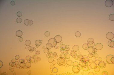 Birçok renkli sabun köpükleri gün batımında turuncu gökyüzünde yüzerler.