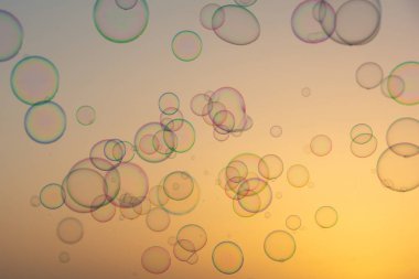 Birçok renkli sabun köpükleri gün batımında turuncu gökyüzünde yüzerler.