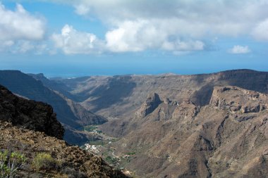 İspanya 'nın Kanarya Adası' ndaki vadide küçük bir köye sahip dağlar. Mavi gökyüzü ve bulutlarla kaplı.