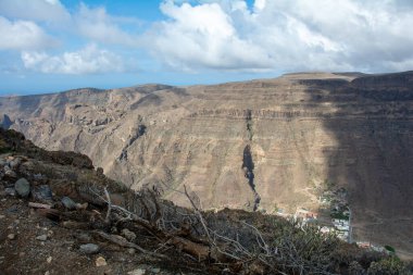 İspanya 'nın Kanarya Adası' ndaki vadide küçük bir köye sahip dağlar. Mavi gökyüzü ve bulutlarla kaplı.