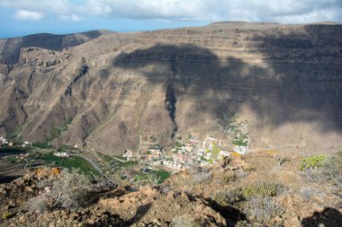 İspanya 'nın Kanarya Adası' ndaki vadide küçük bir köye sahip dağlar. Mavi gökyüzü ve bulutlarla kaplı.
