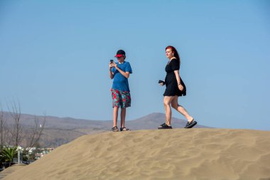 İki genç kum tepeciğinde cep telefonlarıyla duruyorlardı. Çocuk akıllı telefonuna bakıyordu.