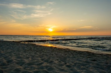 Orang - Okyanusun üzerinde kırmızı gün batımı, kumsalda ve tahta direkler ve martılardan oluşan dalgalı sularda