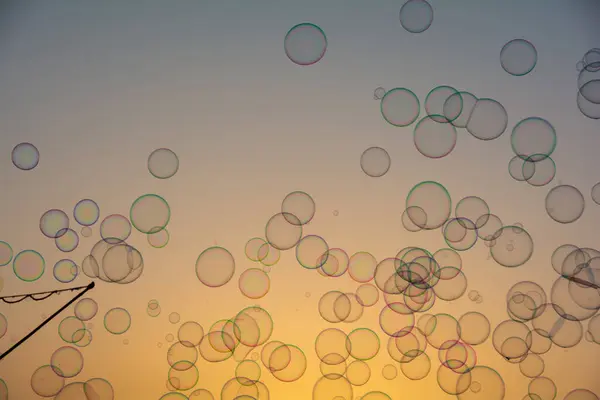 Lots of colorful soap bubbles floating in the orange sky at sunset with soap bubble stick