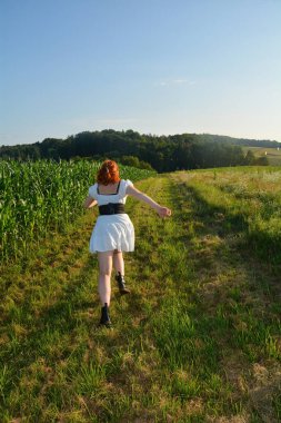 Beyaz kısa elbiseli güzel bir kadın, arkadan, yeşil doğada dışarı koşuyor.