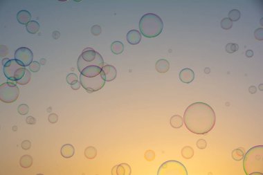Birçok renkli sabun köpükleri gün batımında turuncu gökyüzünde yüzerler.