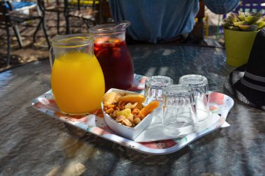 Soğuk sangria ve cam sürahilerde soğuk portakal suyu, masada bardak ve fındık sıcak bir yaz gününde terasta servis edilir.