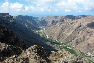 İspanya 'nın Kanarya Adası' ndaki vadide küçük bir köye sahip dağlar. Mavi gökyüzü ve bulutlarla kaplı.