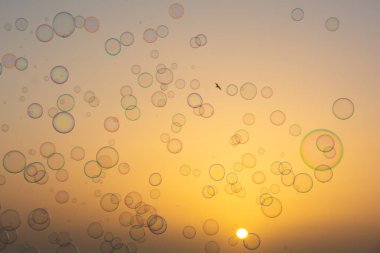 Birçok renkli sabun köpükleri gün batımında turuncu gökyüzünde yüzerler.