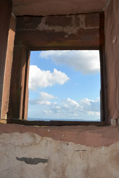 View through an old castle window on a blue sky with white clouds