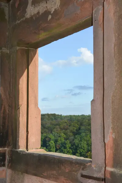 View through an old castle window on a blue sky with white clouds and green landscape