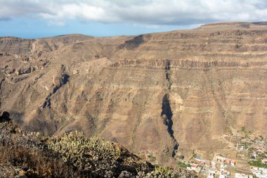 İspanya 'nın Kanarya Adası' ndaki vadide küçük bir köye sahip dağlar. Mavi gökyüzü ve bulutlarla kaplı.
