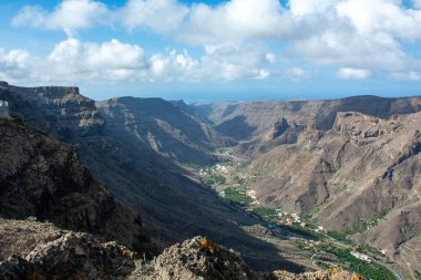 İspanya 'nın Kanarya Adası' ndaki vadide küçük bir köye sahip dağlar. Mavi gökyüzü ve bulutlarla kaplı.