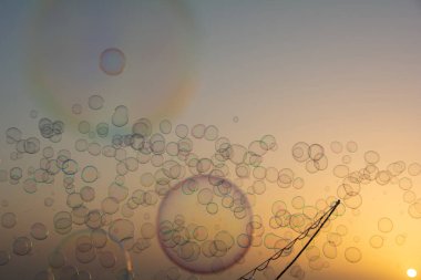 Güneş batarken turuncu gökyüzünde bir sürü renkli sabun köpüğü yüzüyor. Sabun köpüğü çubuğuyla.