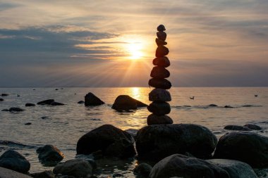 Turuncu gün batımında Baltık Denizi kıyısında bir plajda istiflenmiş taşlar.