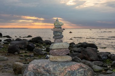 Gün batımında Baltık Denizi kıyısında bir plajda istiflenmiş taşlar.