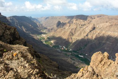 İspanya 'nın Kanarya Adası' ndaki vadide küçük bir köye sahip dağlar. Mavi gökyüzü ve bulutlarla kaplı.