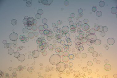 Birçok renkli sabun köpükleri gün batımında turuncu gökyüzünde yüzerler.