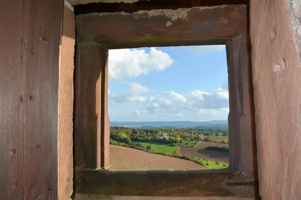View through an old castle window on a blue sky with white clouds and green landscape
