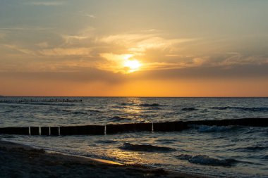 Orang - Okyanusun üzerinde kırmızı gün batımı, kumsalda ve tahta direkler ve martılardan oluşan dalgalı sularda