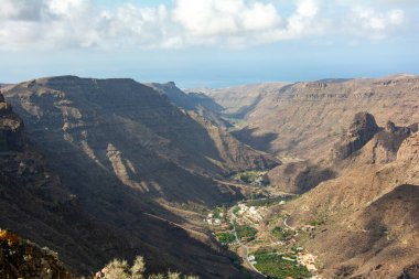 İspanya 'nın Kanarya Adası' ndaki vadide küçük bir köye sahip dağlar. Mavi gökyüzü ve bulutlarla kaplı.