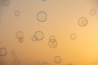 Birçok renkli sabun köpükleri gün batımında turuncu gökyüzünde yüzerler.