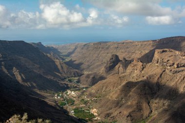 İspanya 'nın Kanarya Adası' ndaki vadide küçük bir köye sahip dağlar. Mavi gökyüzü ve bulutlarla kaplı.