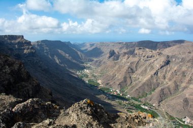 İspanya 'nın Kanarya Adası' ndaki vadide küçük bir köye sahip dağlar. Mavi gökyüzü ve bulutlarla kaplı.
