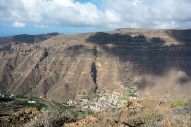 İspanya 'nın Kanarya Adası' ndaki vadide küçük bir köye sahip dağlar. Mavi gökyüzü ve bulutlarla kaplı.