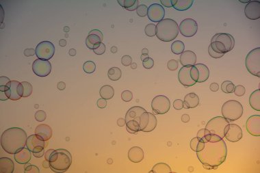 Birçok renkli sabun köpükleri gün batımında turuncu gökyüzünde yüzerler.