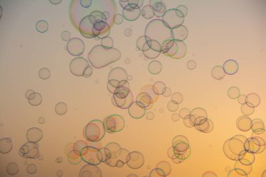 Birçok renkli sabun köpükleri gün batımında turuncu gökyüzünde yüzerler.