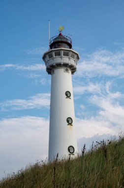 Yaklaşma. 28 metre yüksekliğindeki deniz feneri J.C.J. Egmond 'daki van Speijk aan Zee, Kuzey Hollanda, Hollanda, kumsaldaki kum tepeleri, mavi gökyüzü ve bulutlar