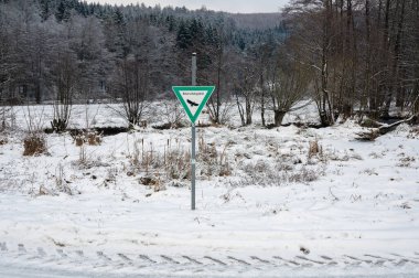 Winter landscape with lots of snow, trees, dirt road and a sign with the inscription 