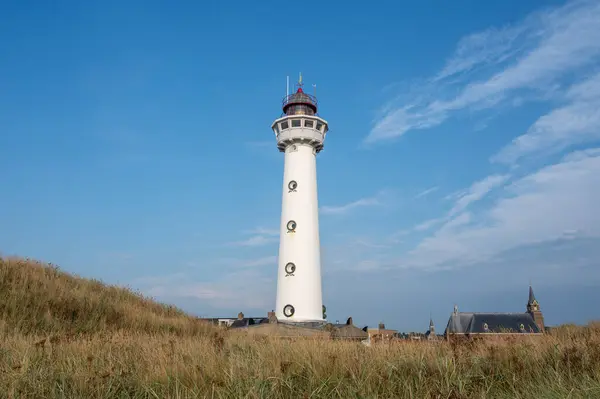Yaklaşma. 28 metre yüksekliğindeki deniz feneri J.C.J. Egmond 'daki van Speijk aan Zee, Kuzey Hollanda, Hollanda Katolik St. Agnes Kilisesi, sahil çimenleri ve kum tepeleriyle