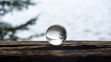 Glass ball on a wood on a cold winter day, with reflections of trees and snow in the glass clipart