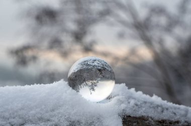 Soğuk bir kış gününde kar altında yatan cam top, camda karla kaplı manzaranın yansımaları.